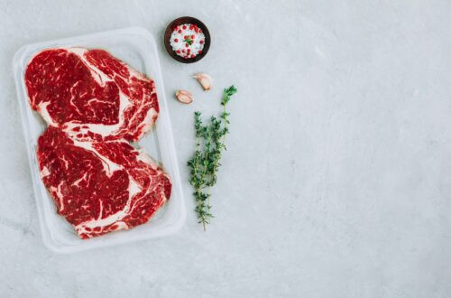 Steak de bœuf haché dans un emballage sous vide avec assaisonnements sur fond de pierre grise, vue du dessus, espace de copie