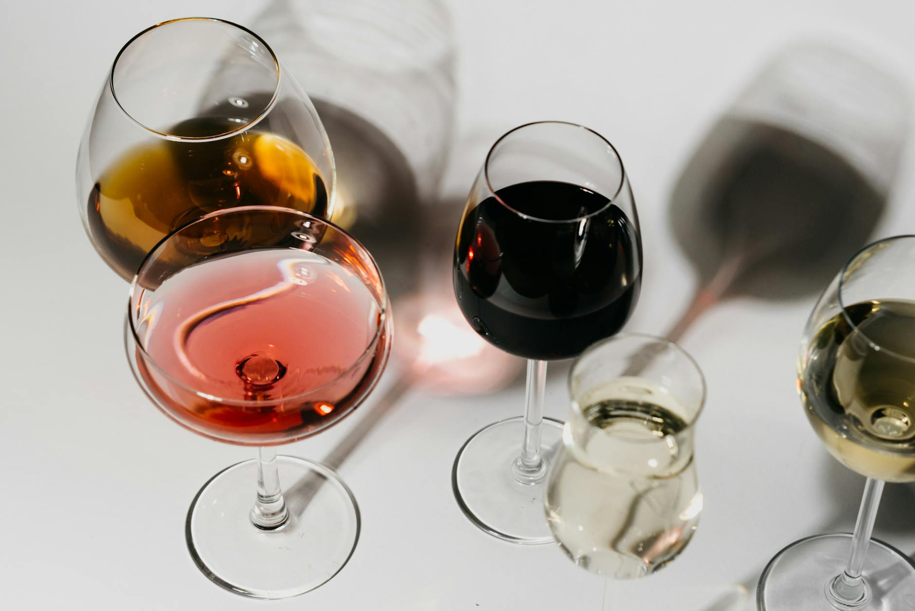 Une variété de verres à vin sur une surface blanche propre, présentant différents types et couleurs de vin.