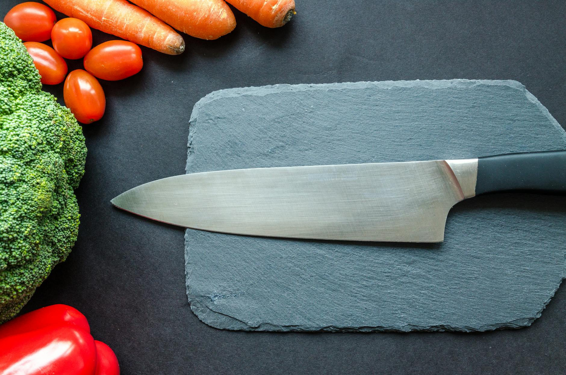 Gros plan de légumes frais avec un couteau de chef sur une planche rustique.